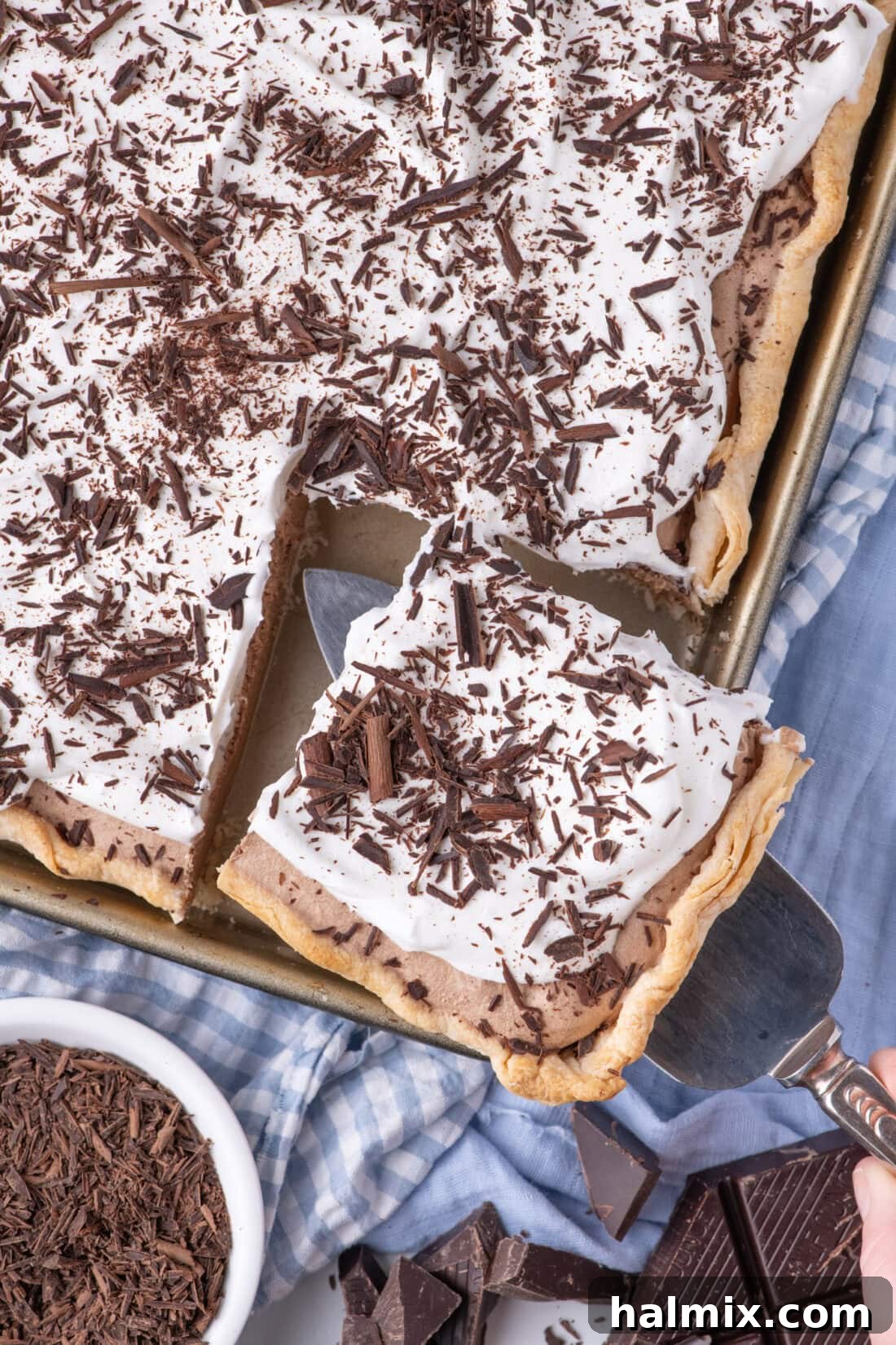 A slice of French Silk Slab Pie being carefully removed from the pan, revealing the smooth chocolate filling and golden-brown crust.