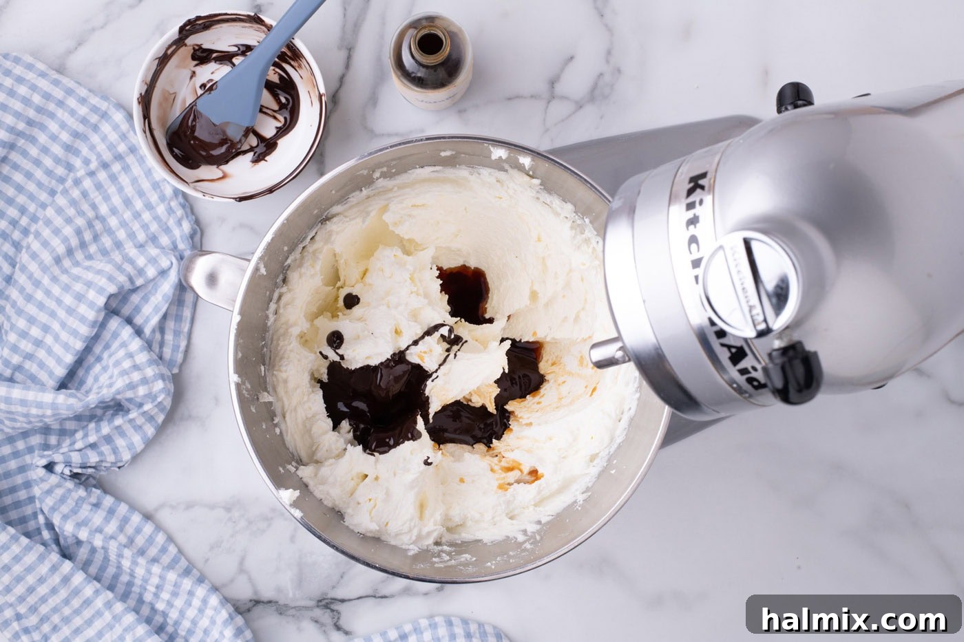 Melted chocolate being added to the creamed butter and sugar mixture in a stand mixer.