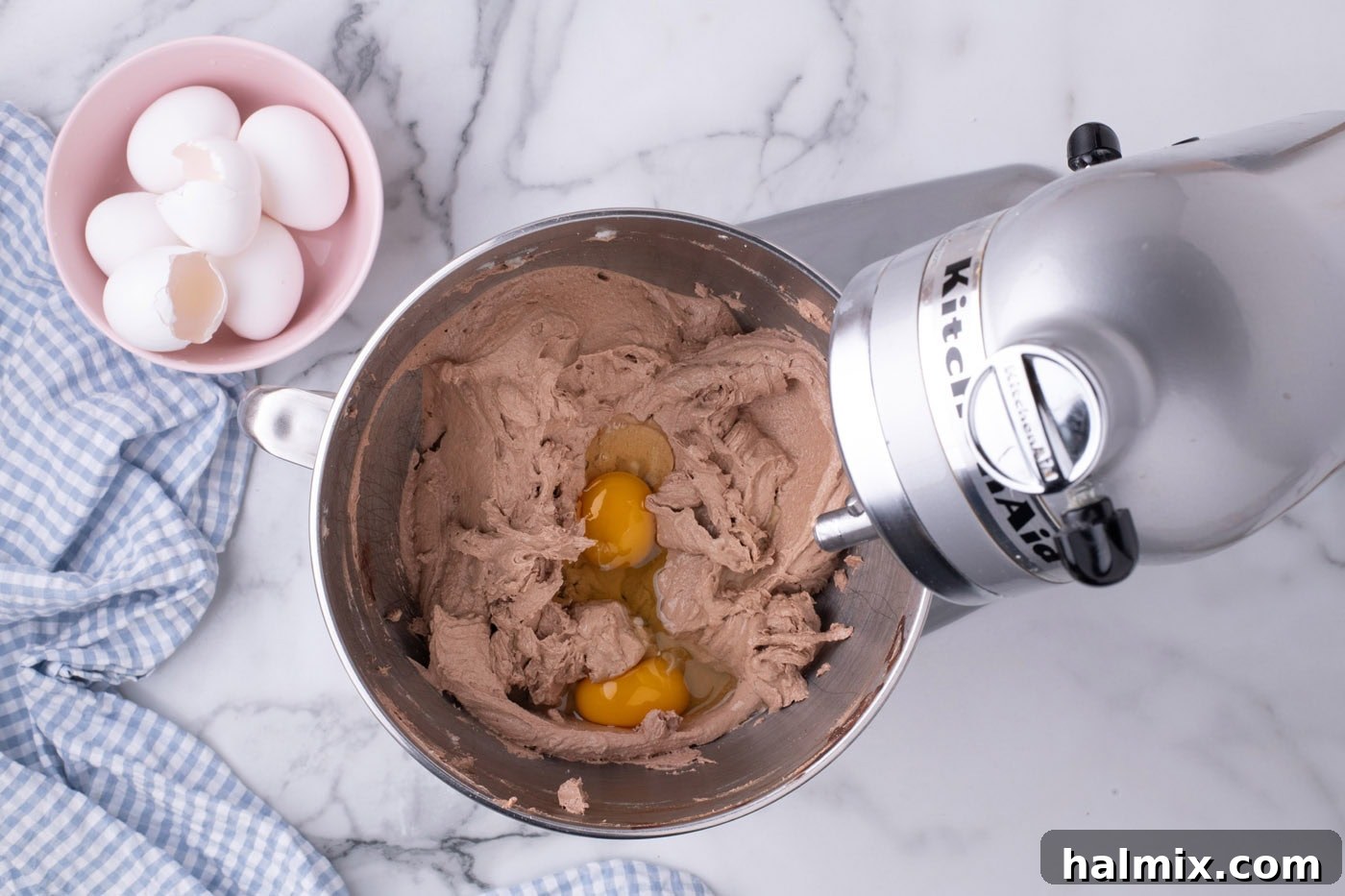 Eggs being added, two at a time, to the pie filling mixture in a stand mixer.