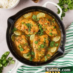 Coconut Chicken in a skillet with rice, herbs and linens on the side, ready to be served.