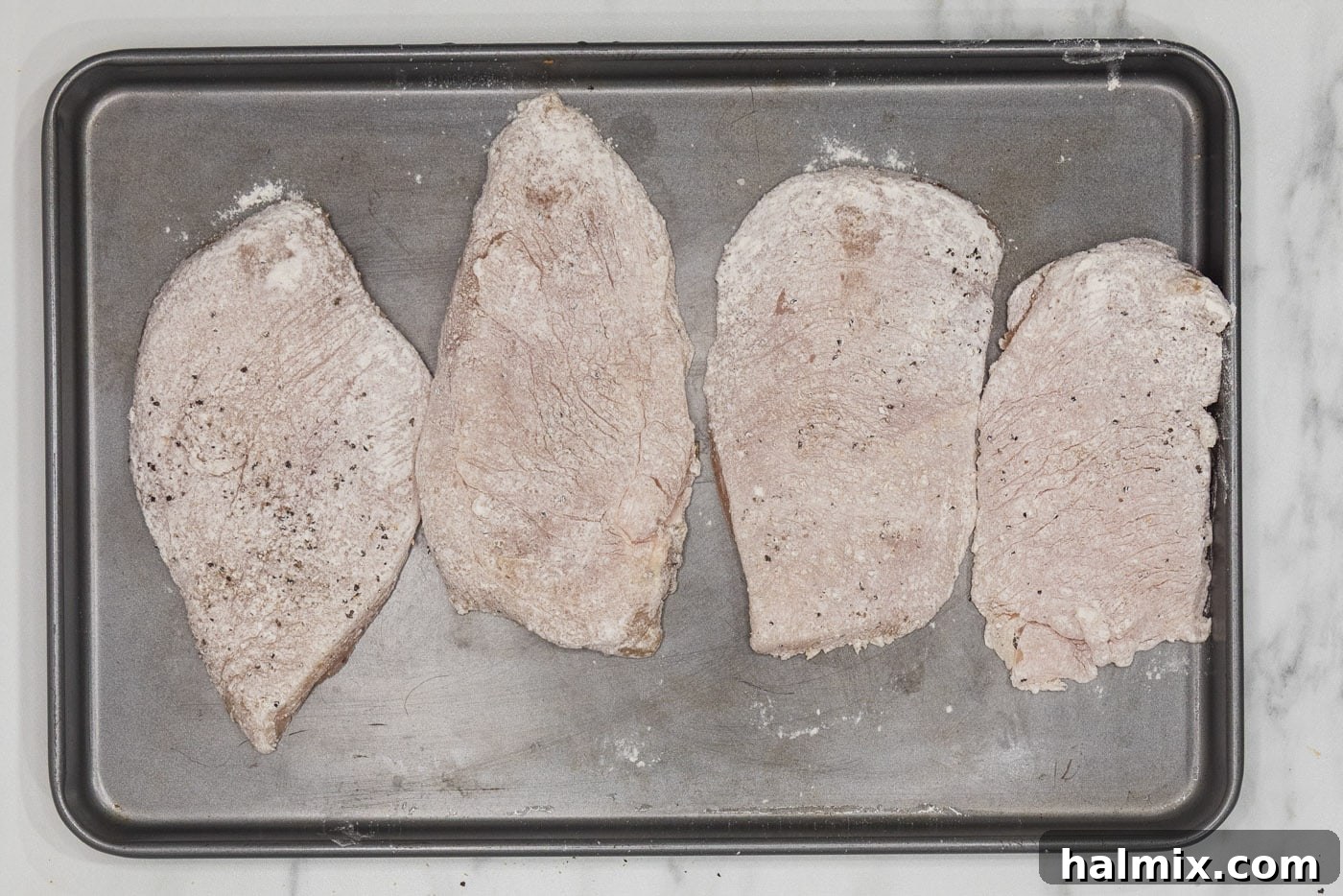 Tropical Coconut Chicken 5 Flour-dredged chicken breasts neatly arranged on a baking sheet, ready for searing.