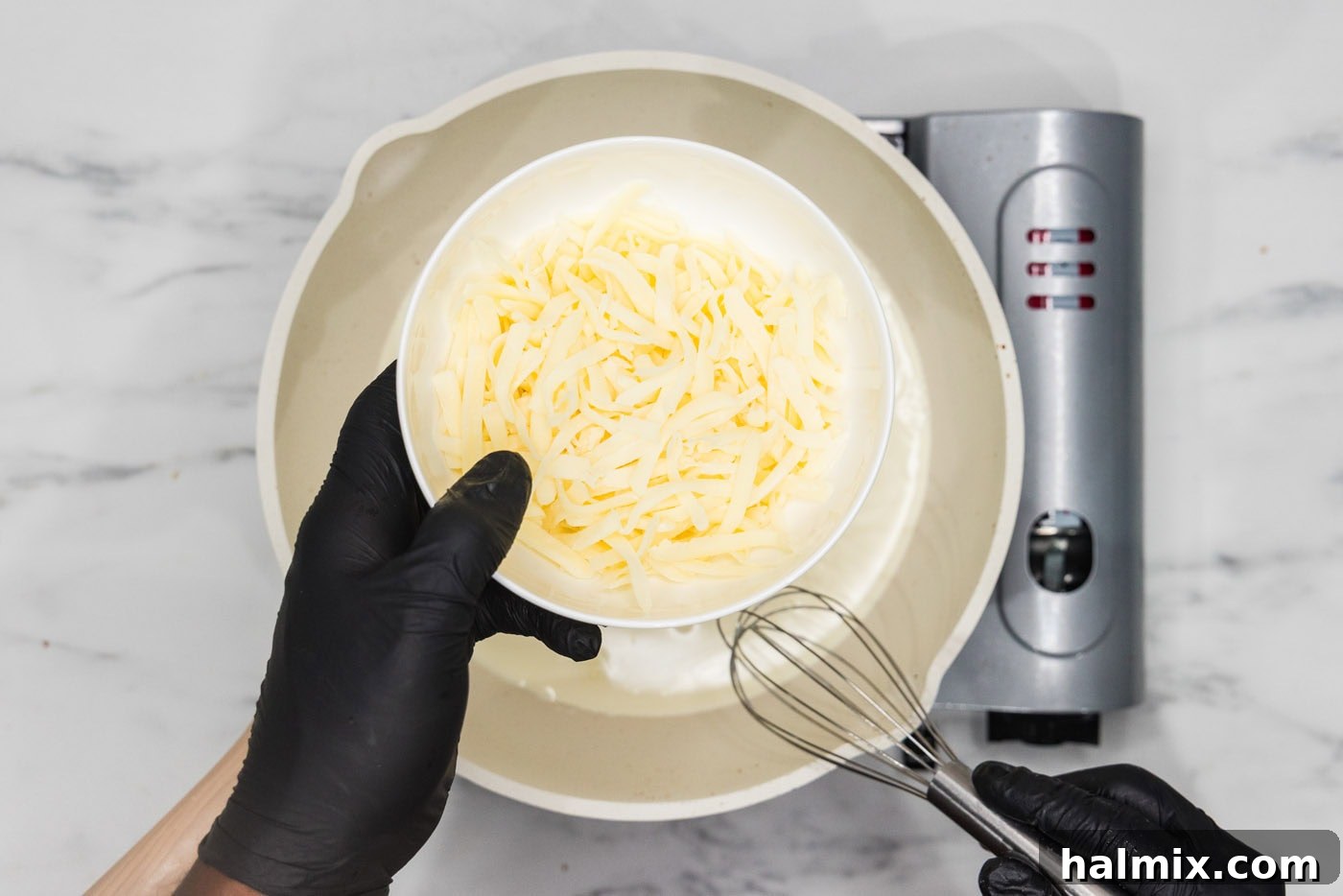 hand holding cheese over a skillet of heavy cream