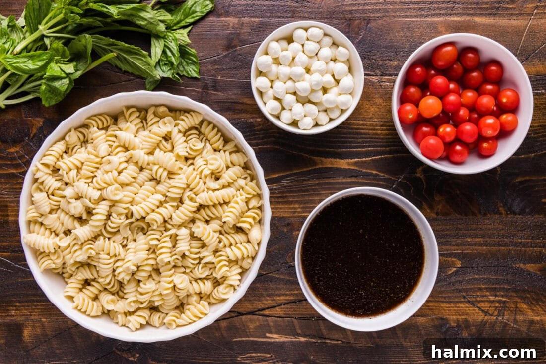 Fresh ingredients for Caprese Pasta Salad including rotini pasta, cherry tomatoes, mozzarella pearls, and basil leaves