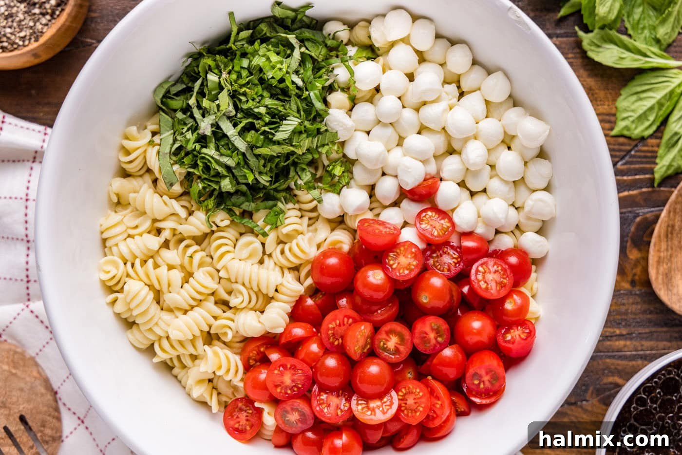 Cooked rotini pasta, halved cherry tomatoes, chopped basil, and fresh mozzarella pearls in a large mixing bowl
