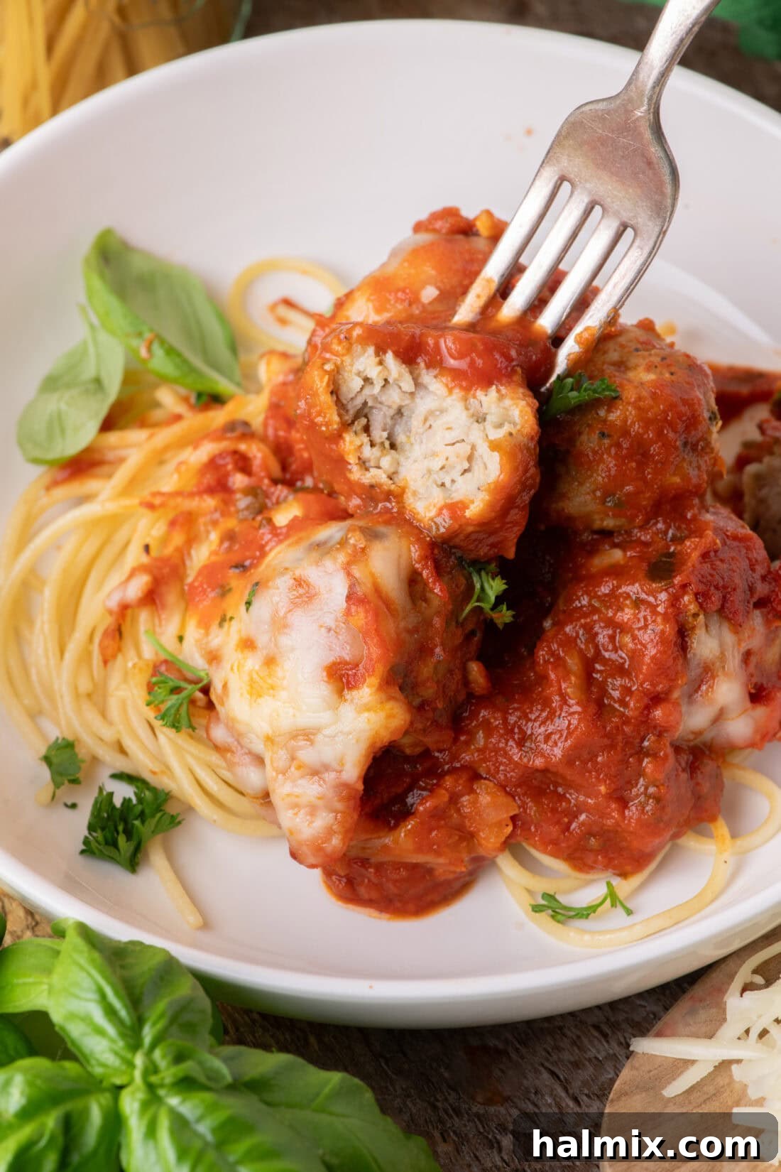 Fork holding half of a Chicken Parmesan Meatball over spaghetti and meatballs
