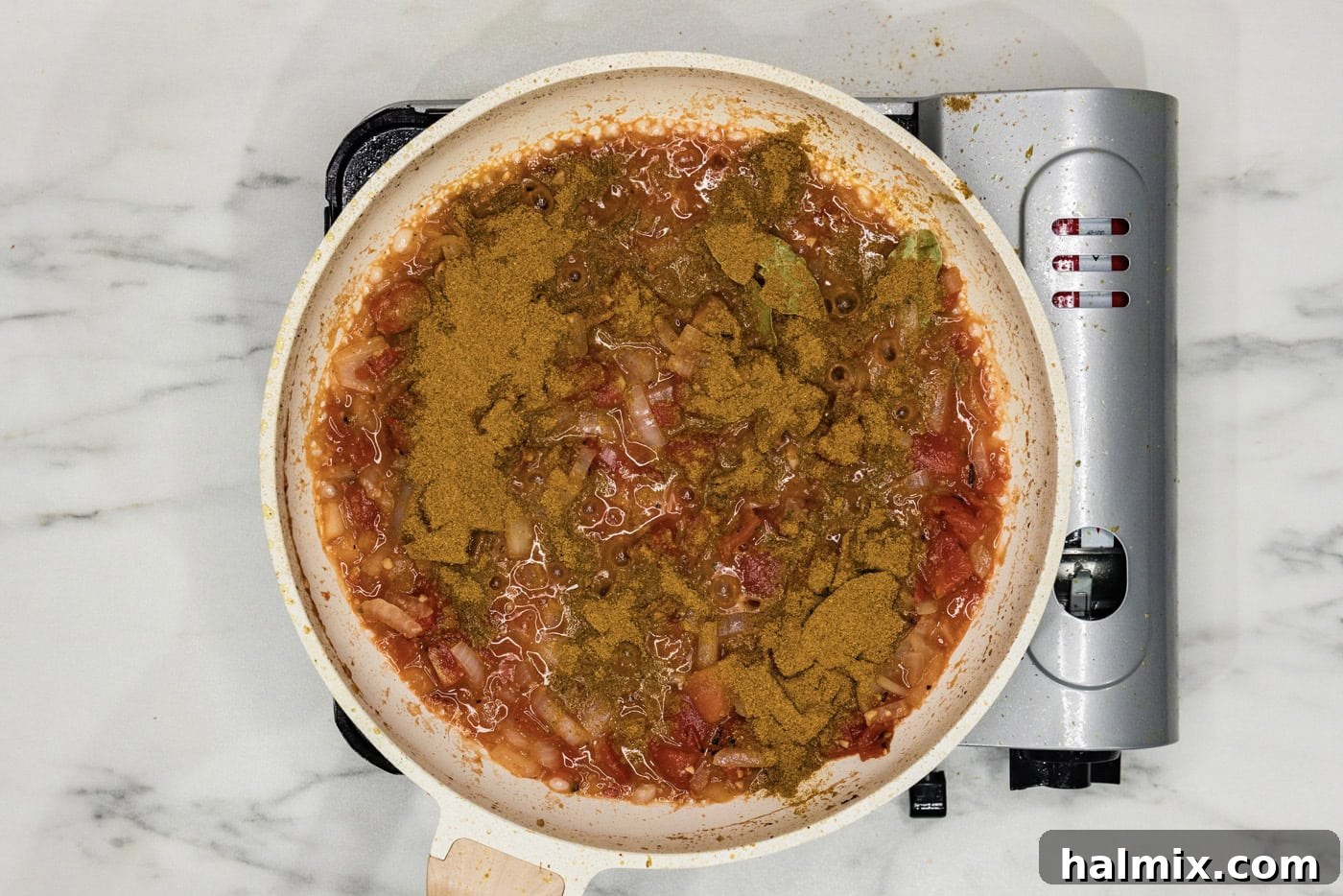 curry powder being stirred into the tomato-based sauce in the skillet