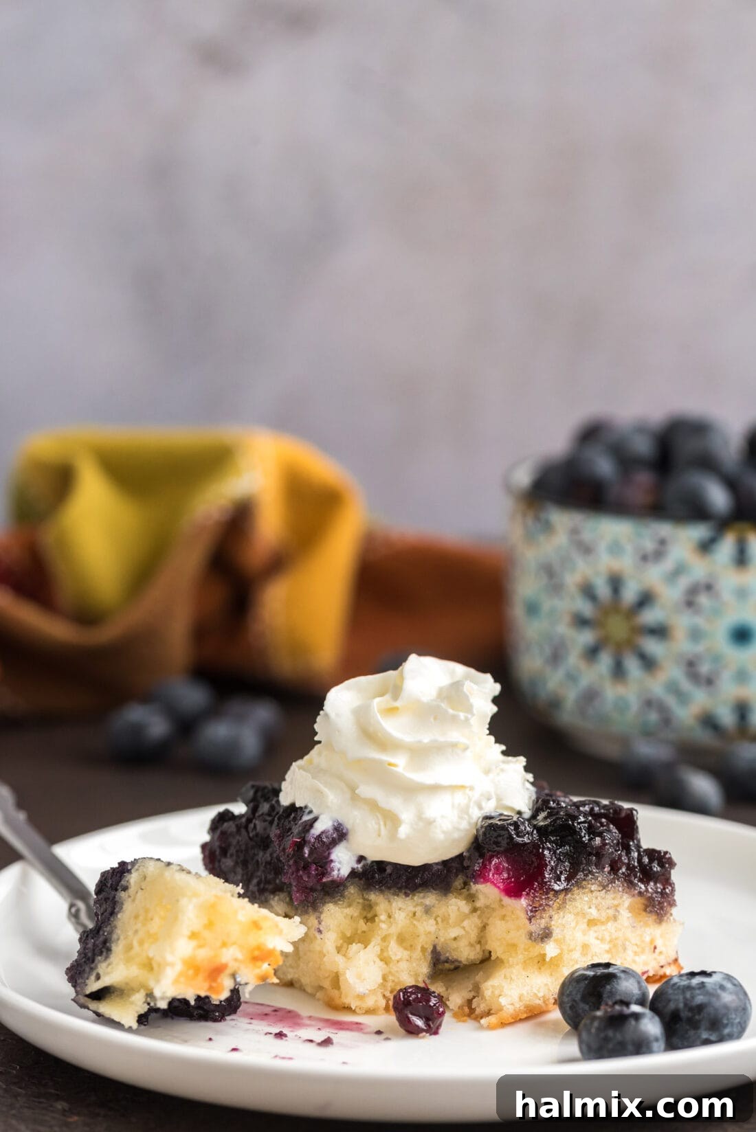 Blueberry Crown Cake 15 A slice of Easy Blueberry Upside Down Cake on a white plate, with a small bite removed, highlighting the tender cake texture and the delicious blueberry topping.