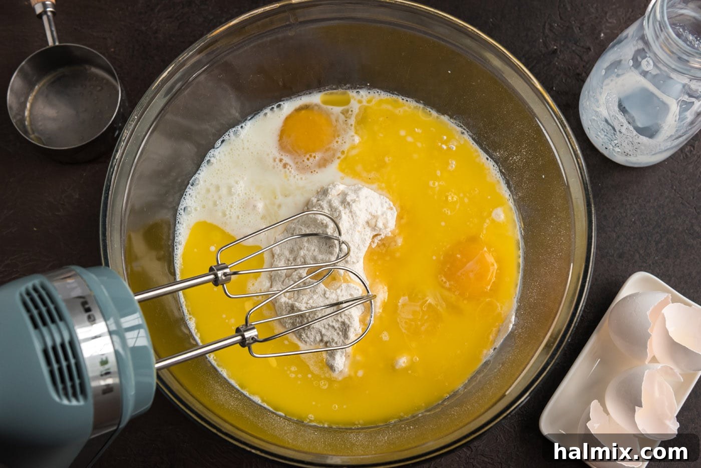 Blueberry Crown Cake 5 A close-up shot of a hand mixer in action, thoroughly blending cake mix with other wet ingredients in a large mixing bowl. The batter appears smooth and well-combined, ready for the next step in baking.