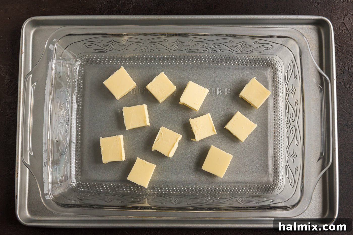 Blueberry Crown Cake 6 Multiple pats of solid butter are meticulously arranged across the bottom of a clear glass baking dish, waiting to be melted for the cake's topping.