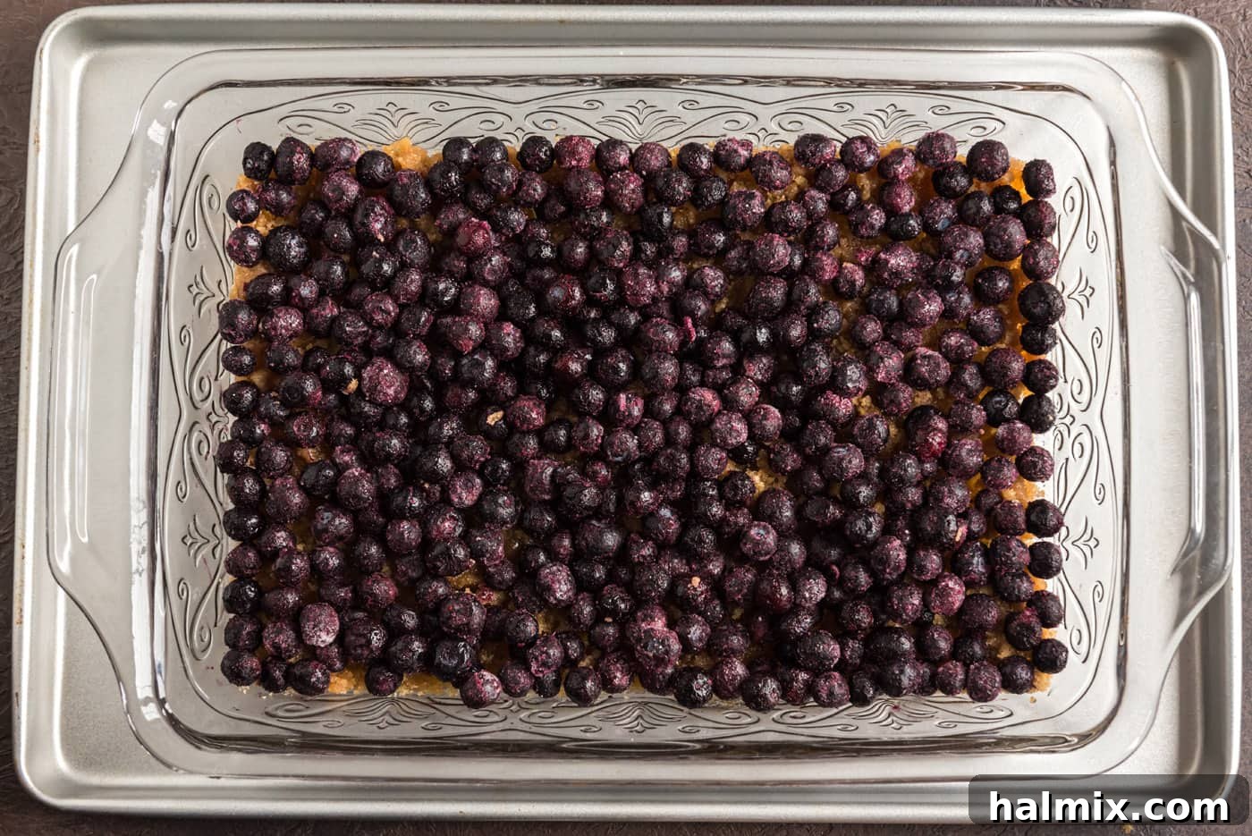 Blueberry Crown Cake 10 A generous layer of fresh, plump blueberries has been added directly on top of the brown sugar and butter mixture in the baking dish, covering the base evenly.