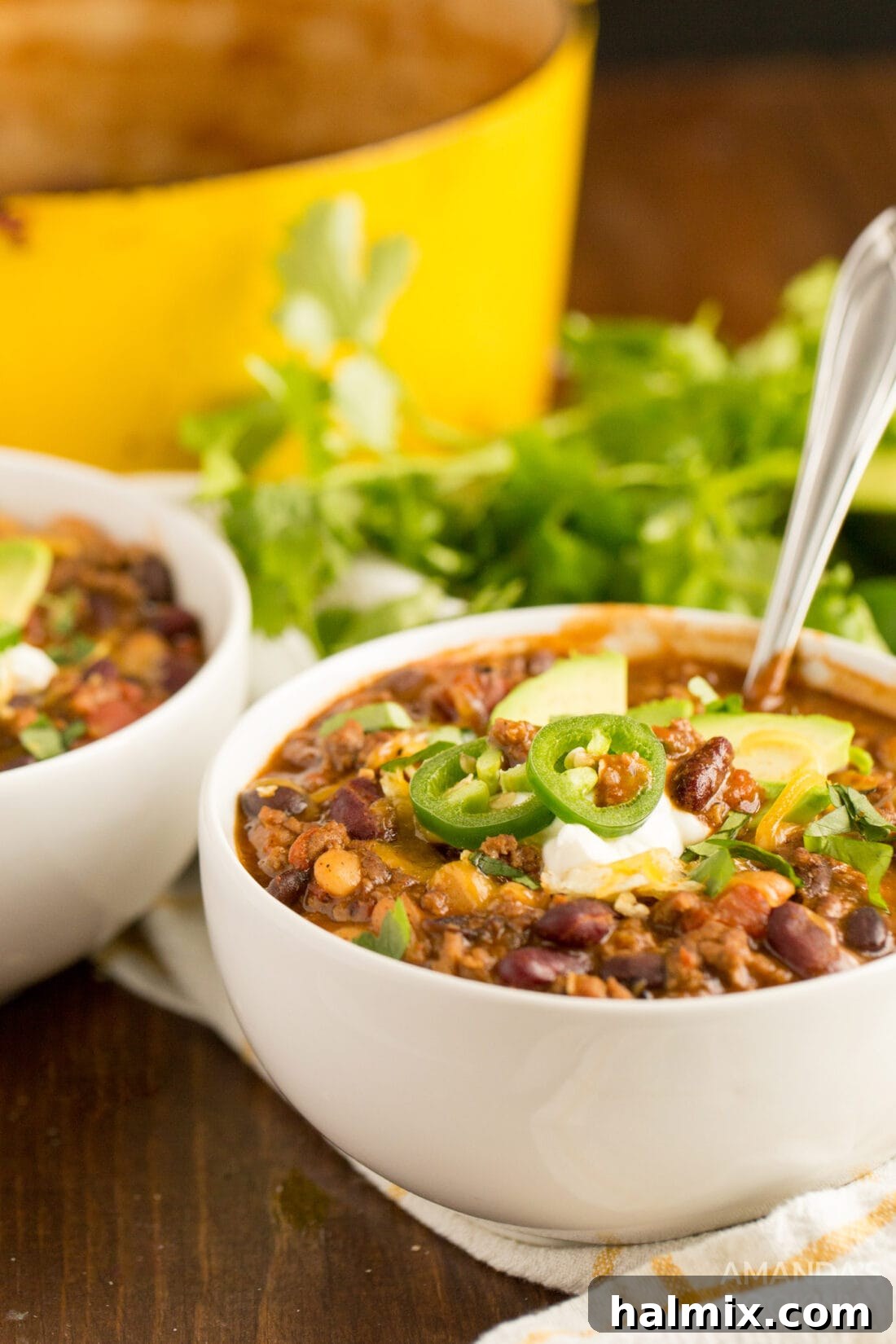 Two bowls of steaming 3 bean chili, topped with sour cream, shredded cheese, and green onions, served on a rustic wooden board.