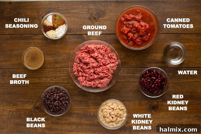 Various ingredients for a 3 bean chili laid out on a wooden table, including canned beans, ground beef, tomatoes, and seasoning ingredients.