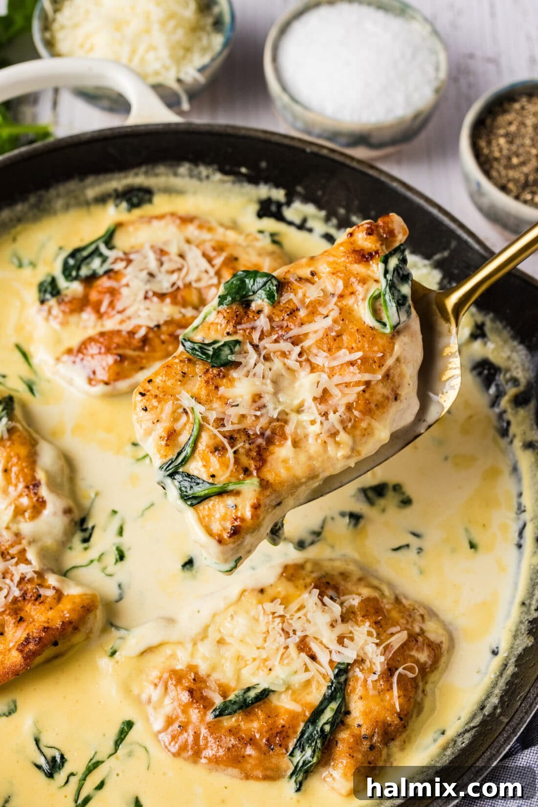 Spatula holding up a piece of Chicken Florentine above a skillet, showcasing the rich sauce and tender chicken