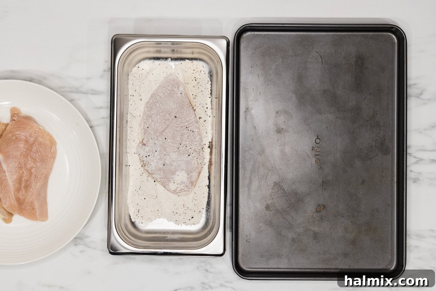 chicken cutlet being pressed into a flour mixture in a breading tray