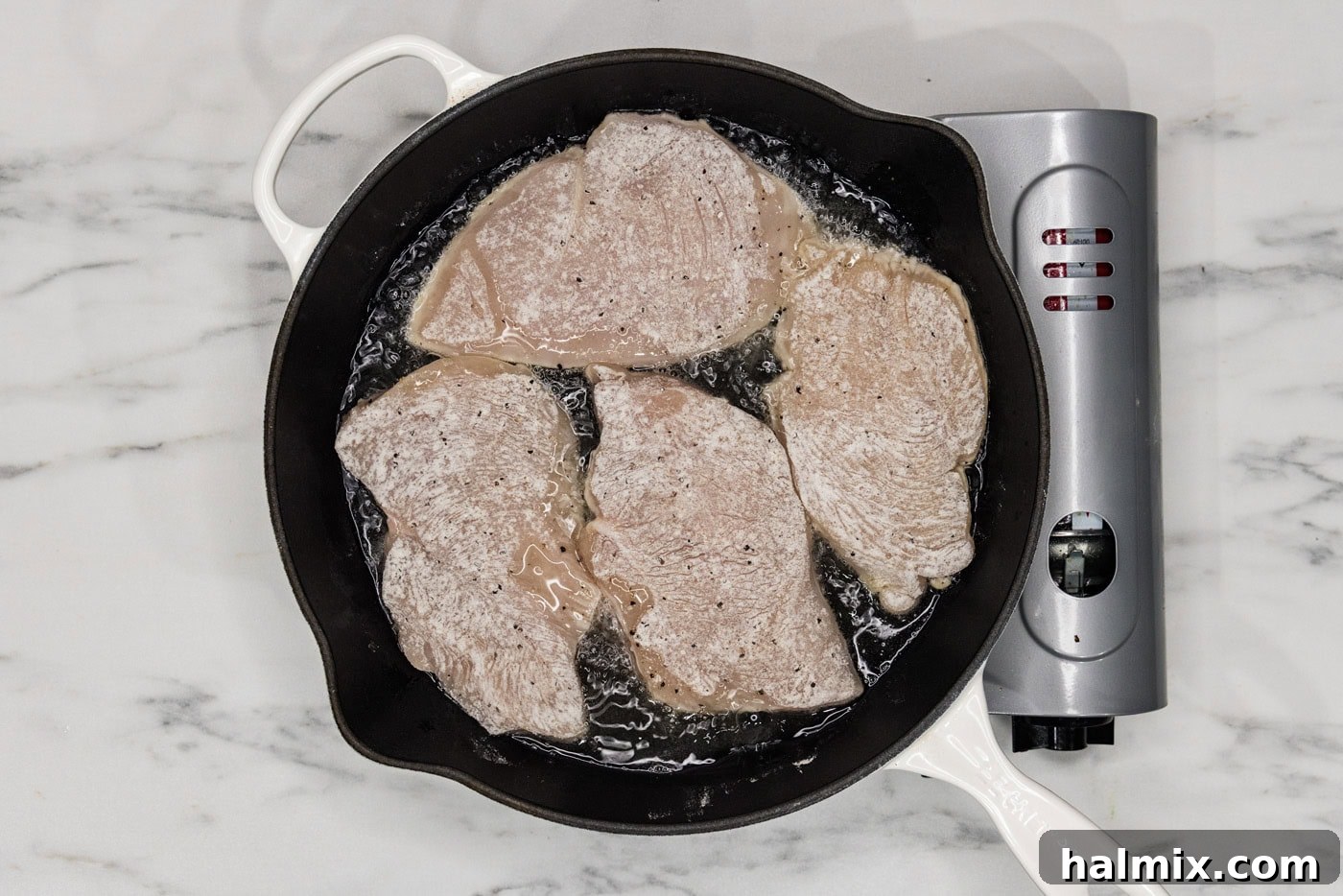 lightly coated chicken cutlets cooking in a cast iron skillet