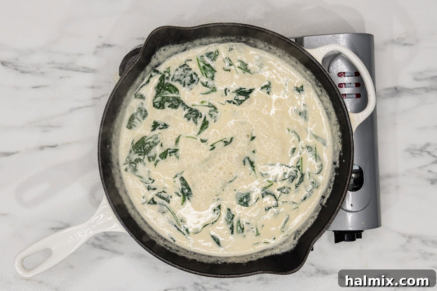 fresh spinach leaves wilting in a creamy sauce in a skillet