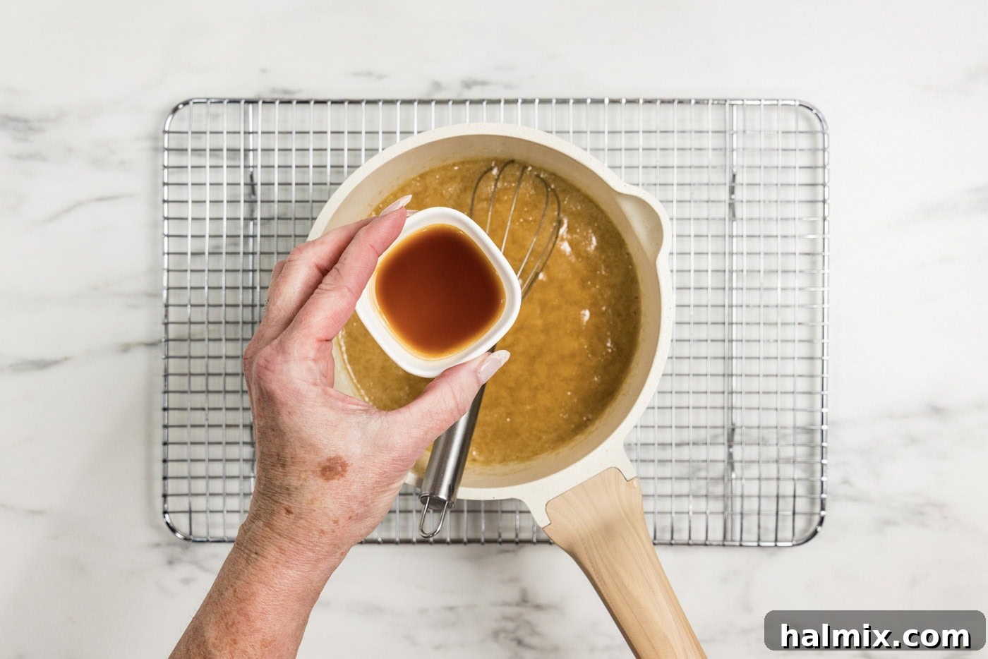 hand holding vanilla over caramel mixture in a saucepan