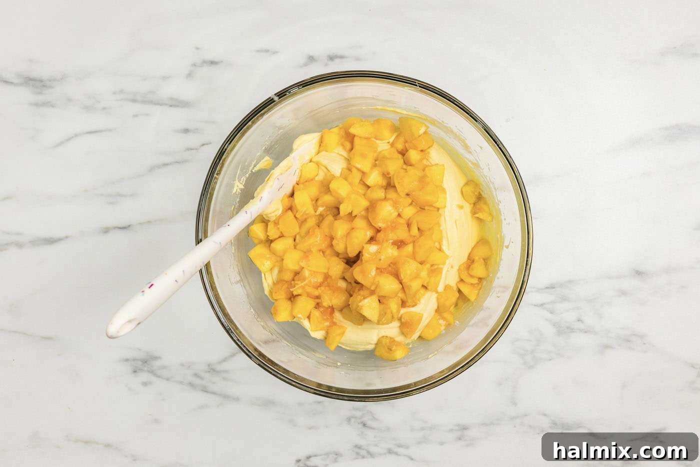 rubber spatula in a bowl with chopped peaches and cake batter