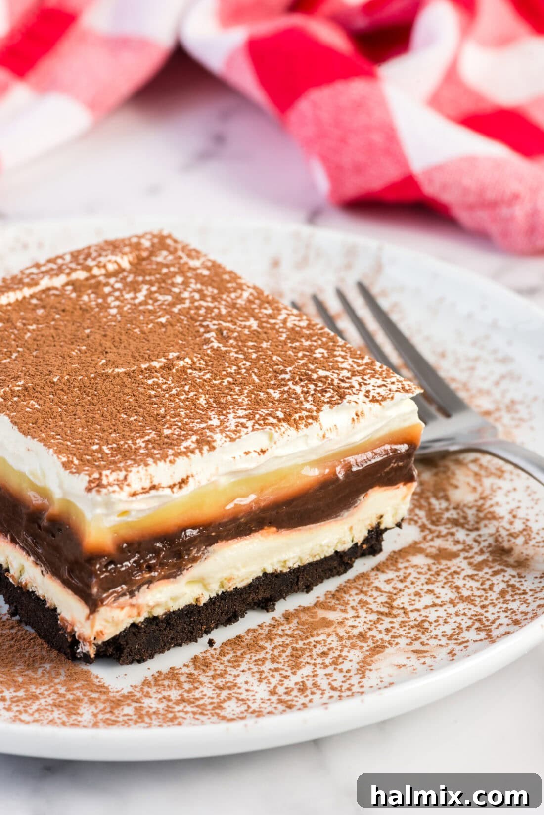 Pure Bliss Pan Dessert 2 A perfectly portioned slice of Sex in a Pan on a white plate, showcasing its distinct layers and a fork ready to dig in.