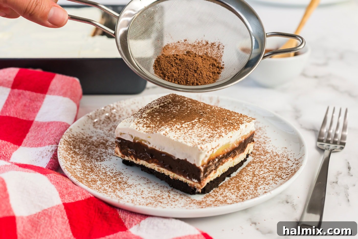 Pure Bliss Pan Dessert 13 A fine dusting of cocoa powder being sifted onto a freshly cut slice of Sex in a Pan, enhancing its chocolate appeal.