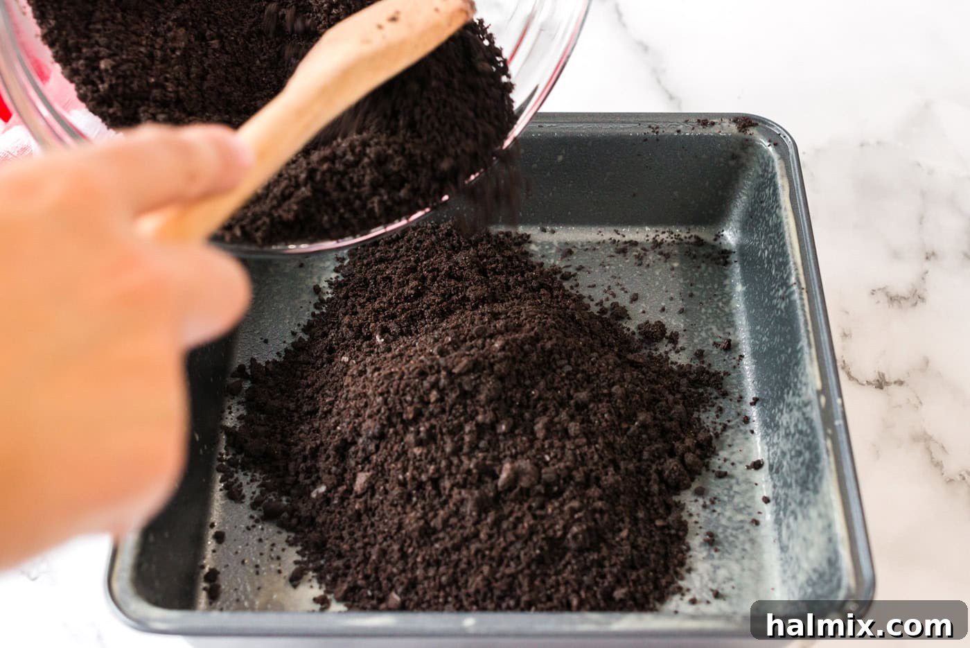 Pure Bliss Pan Dessert 6 The dark chocolate crumb mixture being pressed firmly into a square baking pan, forming the base layer of the dessert.