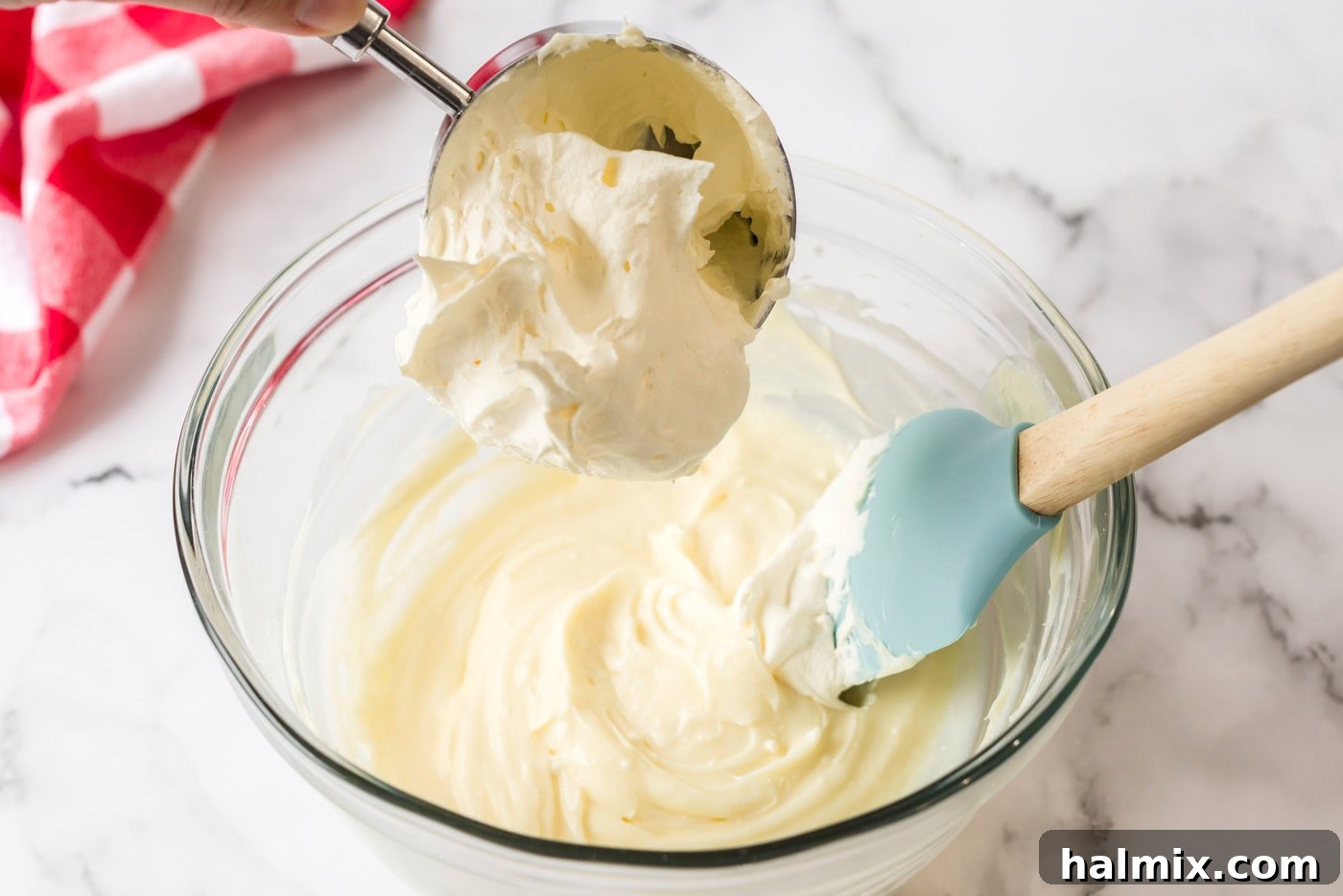 Pure Bliss Pan Dessert 8 A generous dollop of Cool Whip being carefully folded into the light and fluffy cream cheese mixture using a spatula.