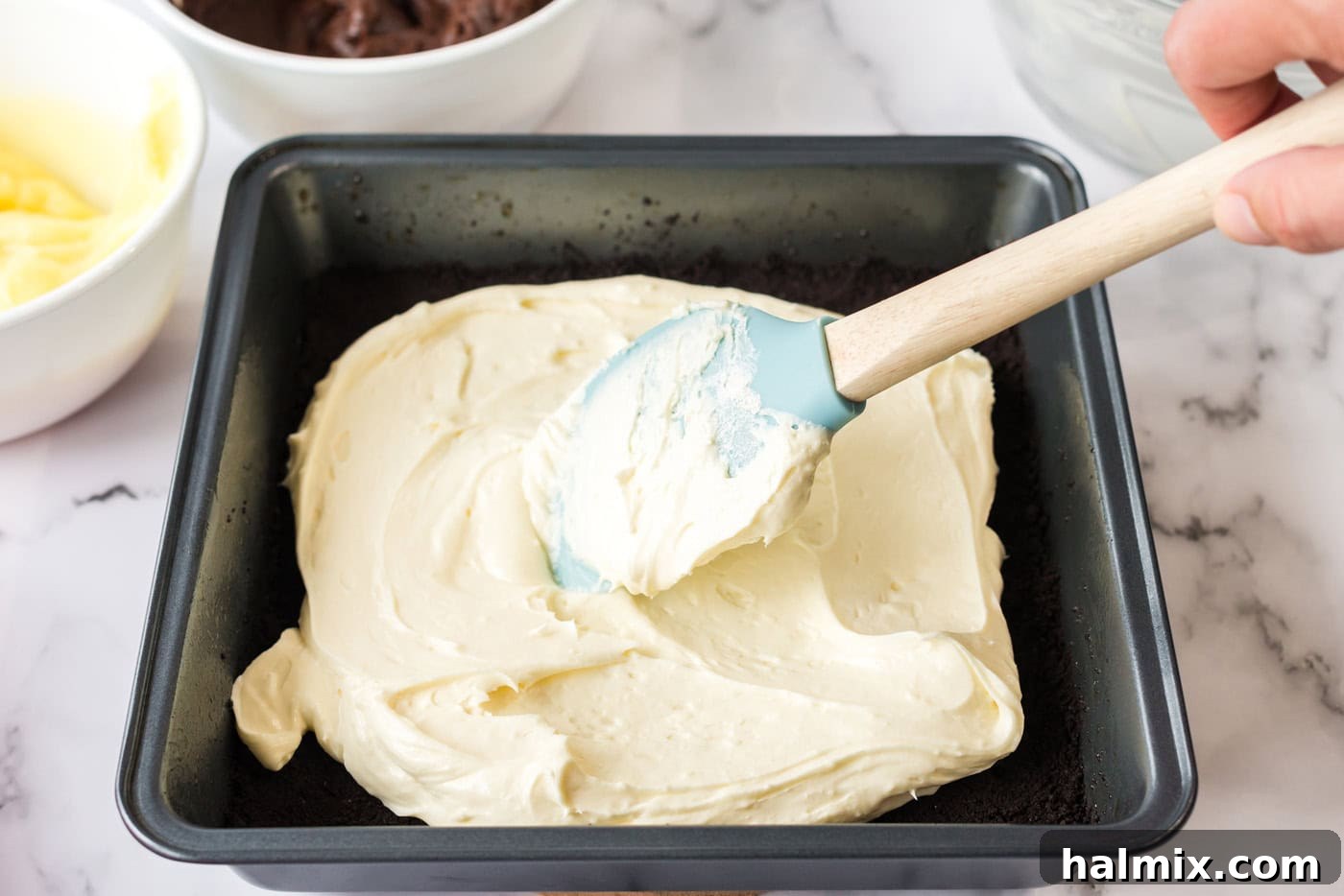 Pure Bliss Pan Dessert 9 The creamy, white cream cheese mixture being meticulously spread across the dark chocolate crust in a baking pan.