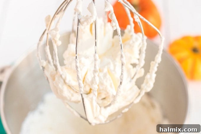 an electric whisk showing stiff peaks of whipped cream in a mixing bowl