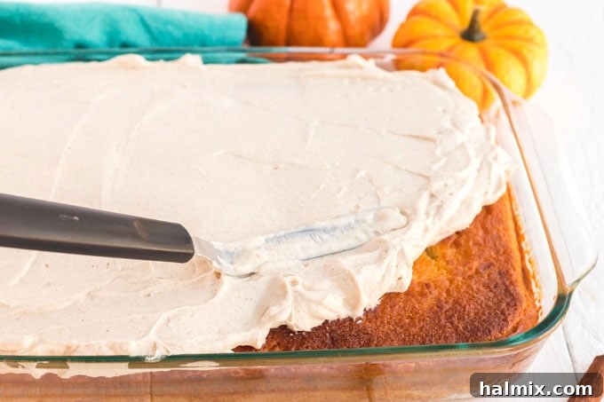 someone spreading the creamy topping evenly over the cooled pumpkin magic cake with a spatula