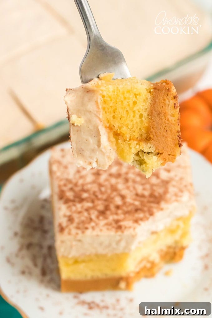 a fork piercing a slice of pumpkin magic cake, showing off the perfectly layered cake, pumpkin, and topping