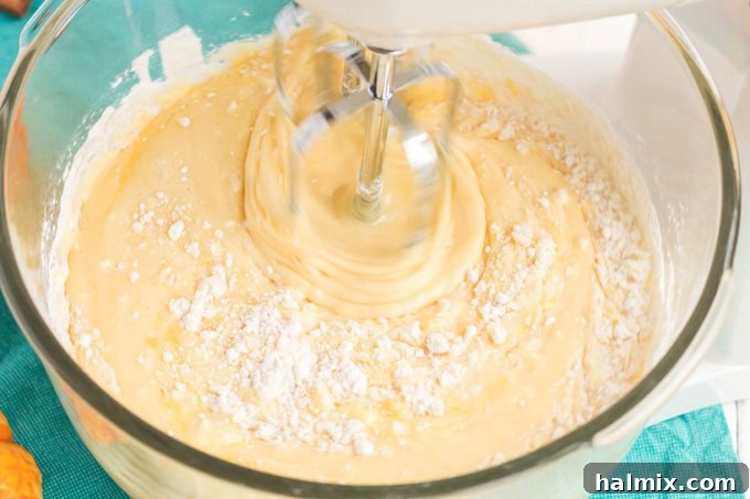 a mixing bowl with yellow cake batter being mixed with an electric mixer
