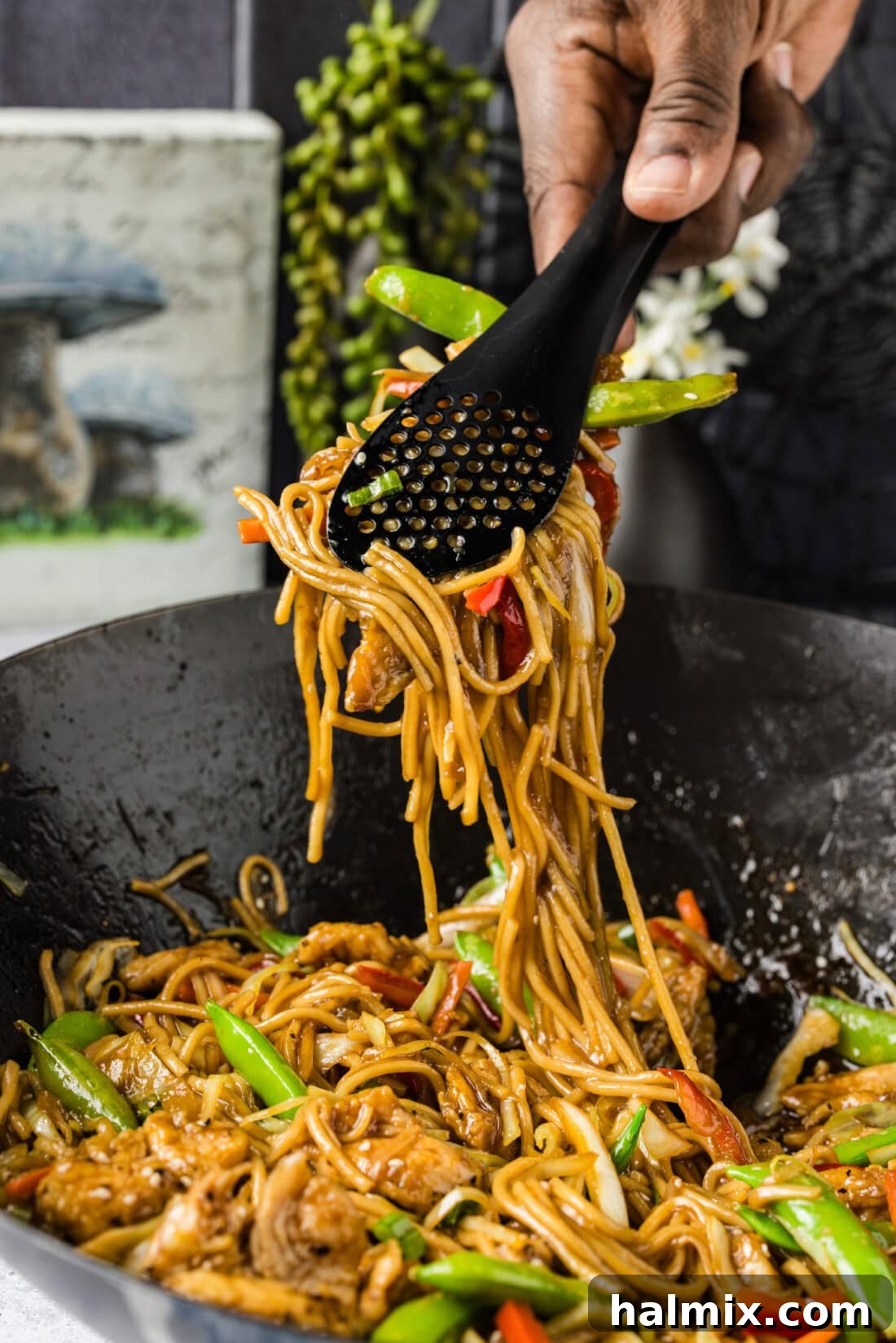 Flavorful Chicken Lo Mein Stir Fry 11 Tongs lifting a generous portion of Chicken Lo Mein from a wok, showcasing the saucy noodles and mixed ingredients.
