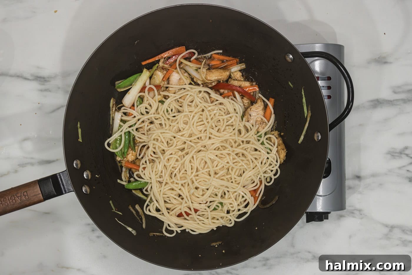Flavorful Chicken Lo Mein Stir Fry 10 Cooked lo mein noodles being added to a skillet with chicken and vegetables, ready to be tossed.