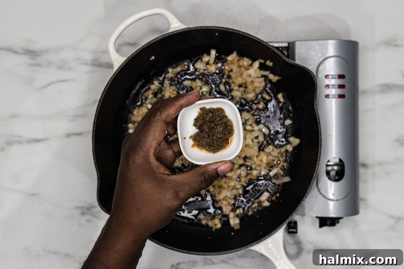 Creamy Sun-Dried Tomato Tuscan Chicken 7 hand holding italian herb base in a small bowl over a skillet of shallots and garlic