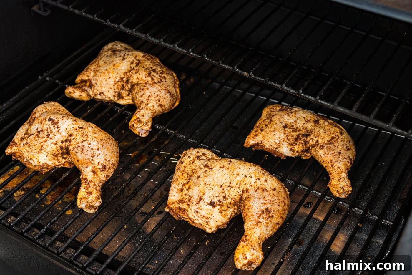 photo of seasoned chicken quarters on smoker grill grates