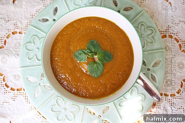 An inviting overhead photo of a beautifully garnished bowl of pumpkin soup, featuring an artistic swirl of cream and a vibrant sprig of fresh parsley, ready to be enjoyed.