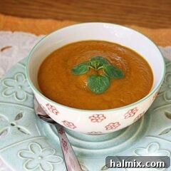 A close up photo of a bowl of pumpkin soup with a spoon on the side.