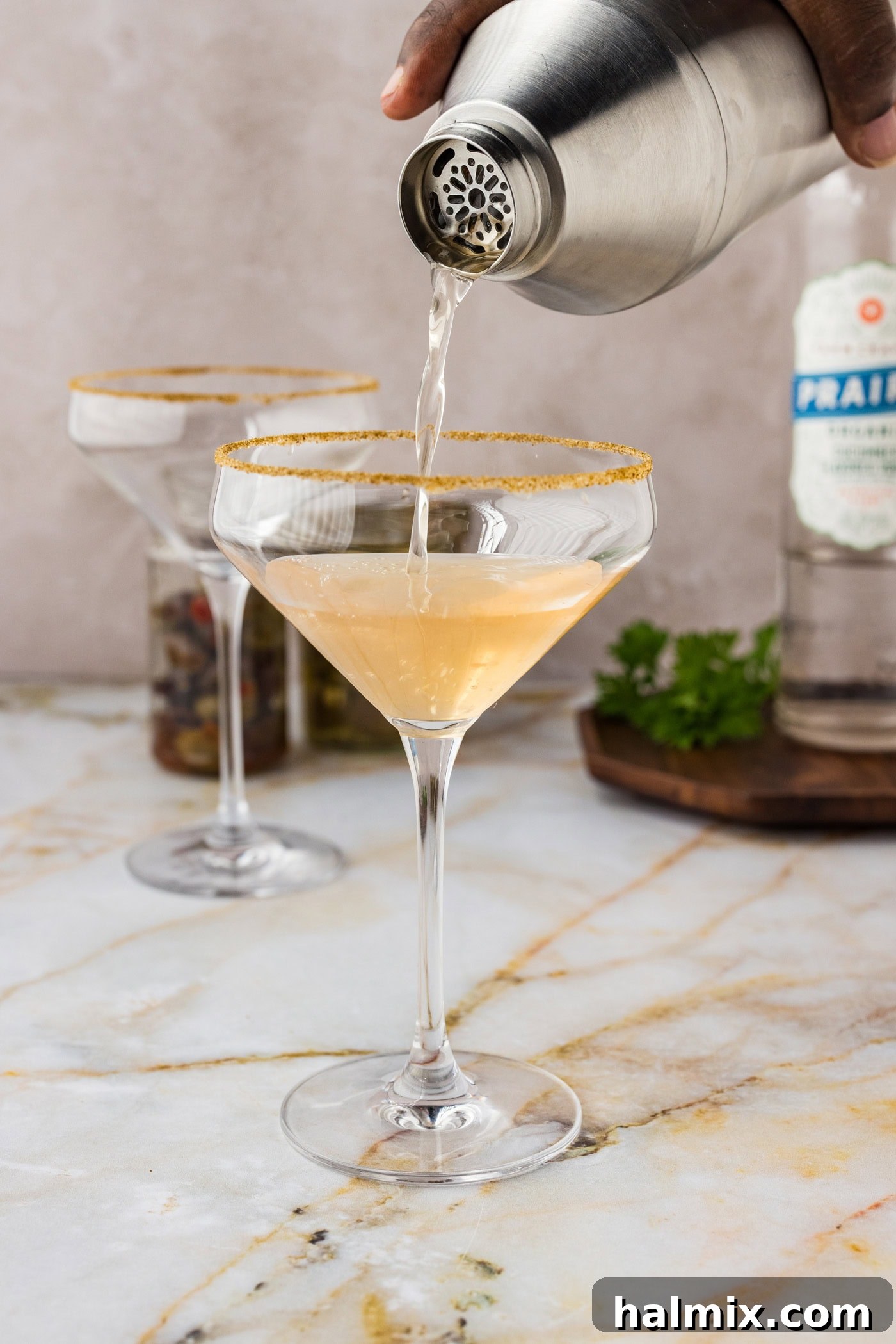 pouring dirty greek martini from a cocktail shaker into a glass