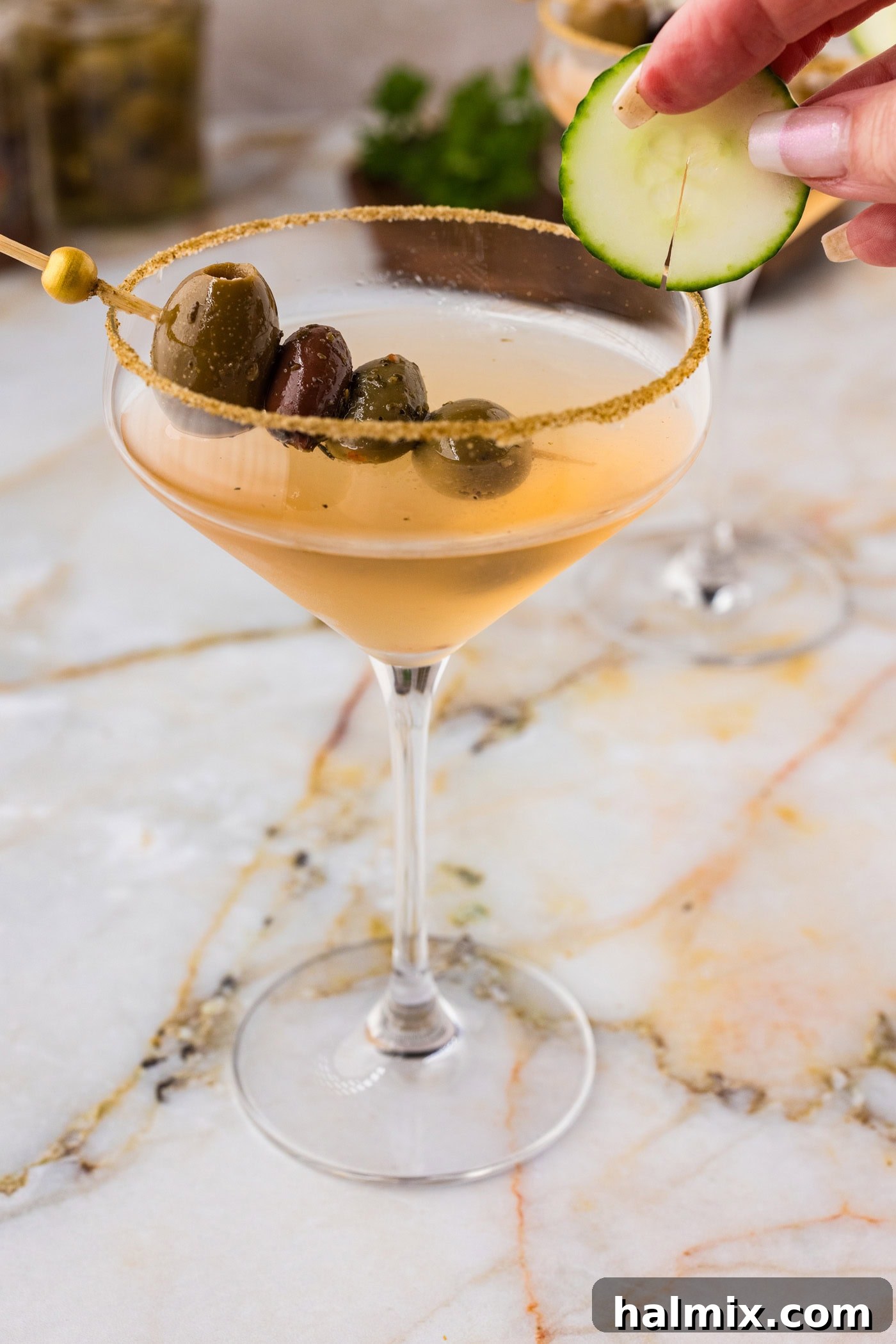 hand adding a cucumber wheel to the side of a dirty greek martini glass