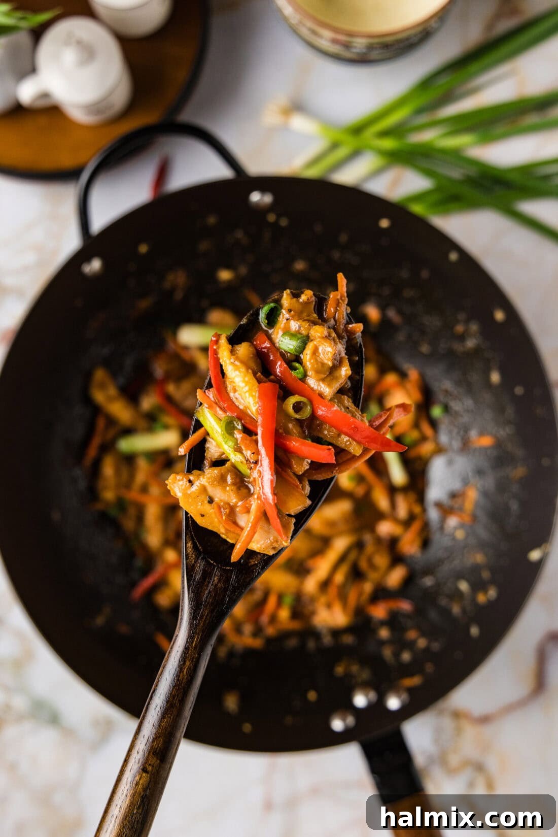 A tantalizing spoonful of Szechuan Chicken, perfectly coated in a glistening sauce, is held above a large wok filled with more of the flavorful dish, showcasing its rich texture and appealing glaze.