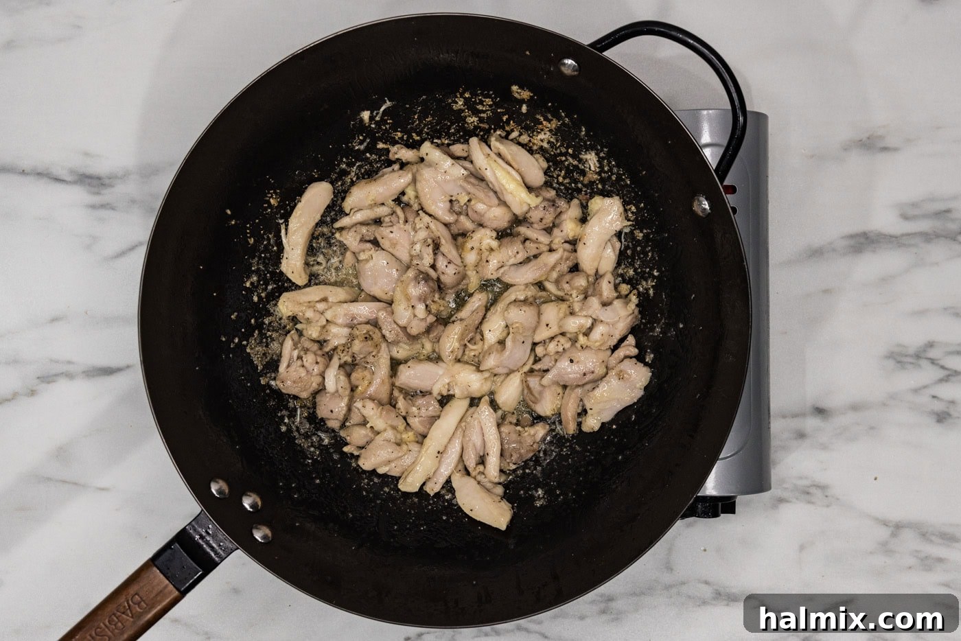 Cooked sliced chicken in a wok with oil, showing a golden brown crust.