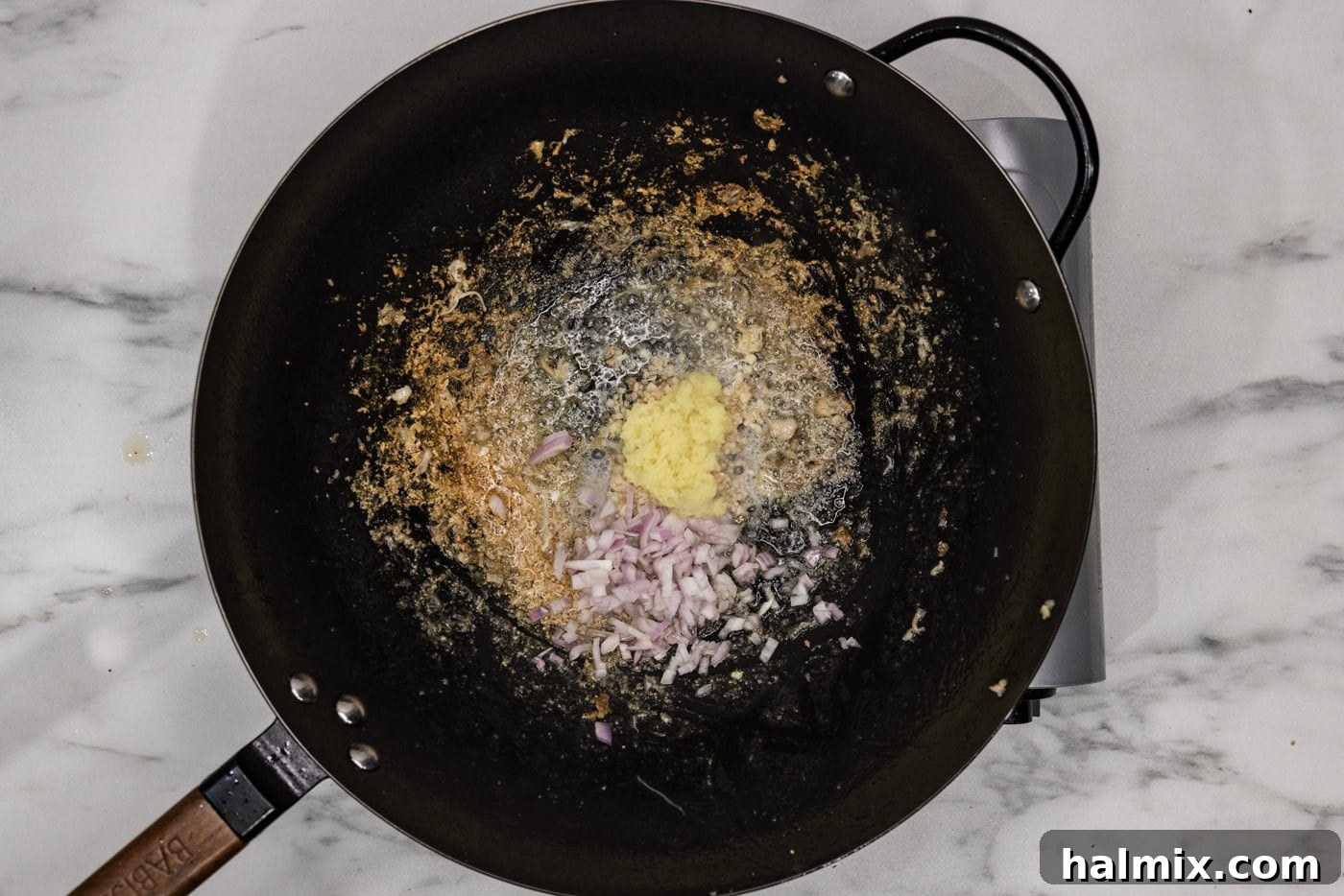 Minced garlic, ginger, and shallots added to a wok, sizzling in oil.