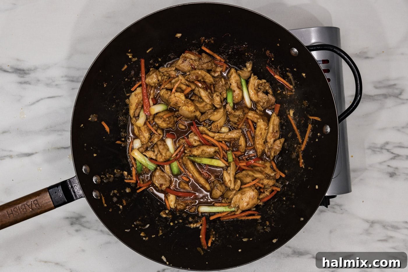 An overhead shot of cooked Szechuan chicken in a wok, richly coated in sauce, with steam rising.