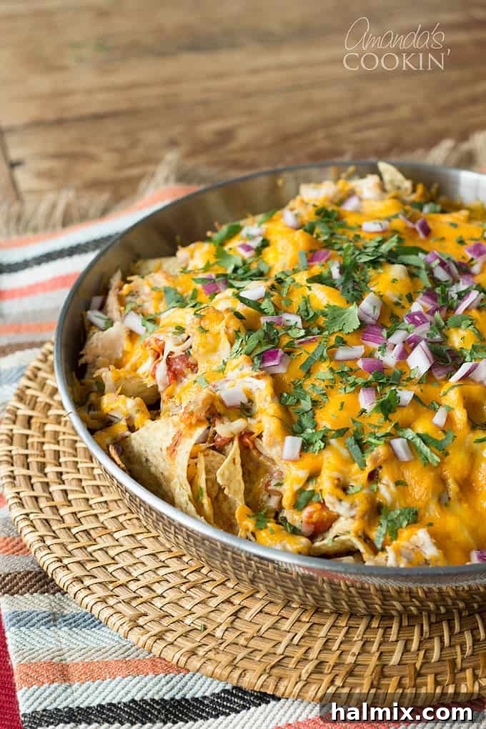 A stainless steel bowl of rotisserie chicken nachos resting on a wicker place mat, showcasing the crispy chips, melted cheese, and shredded chicken.