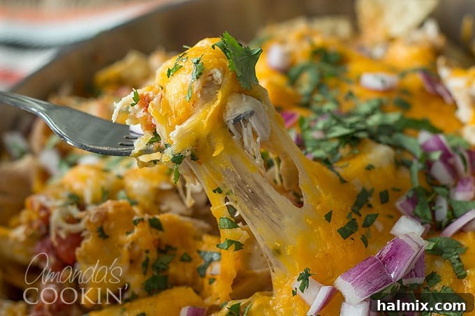 A close up of a forkful of chicken nachos with a long cheese pull, emphasizing the gooey texture.