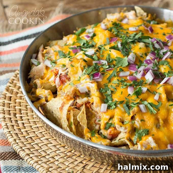 A stainless steel bowl of rotisserie chicken nachos resting on a wicker place mat, ready to be served.