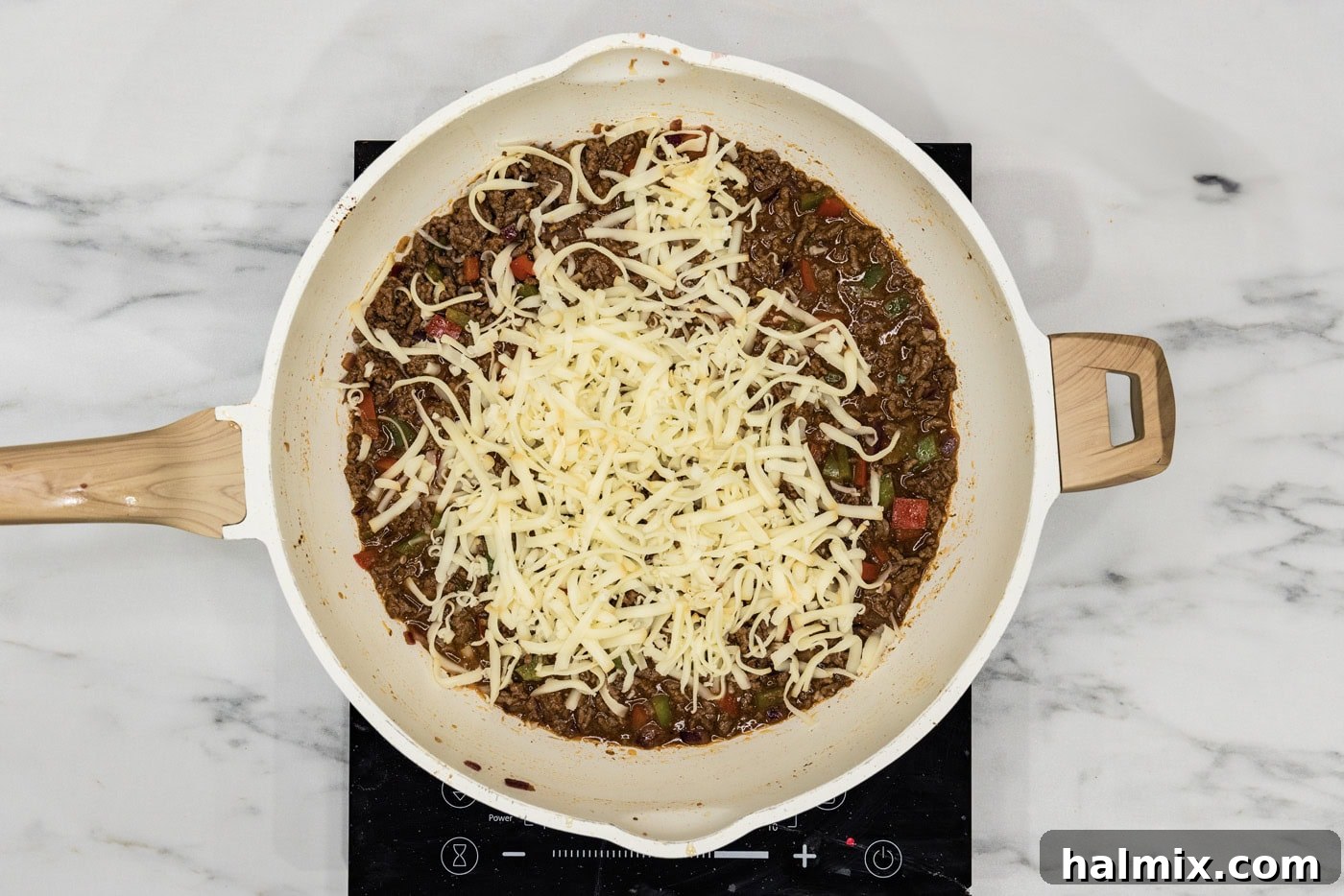 shredded provolone cheese on top of philly cheesesteak sloppy jooe mixture in a skillet