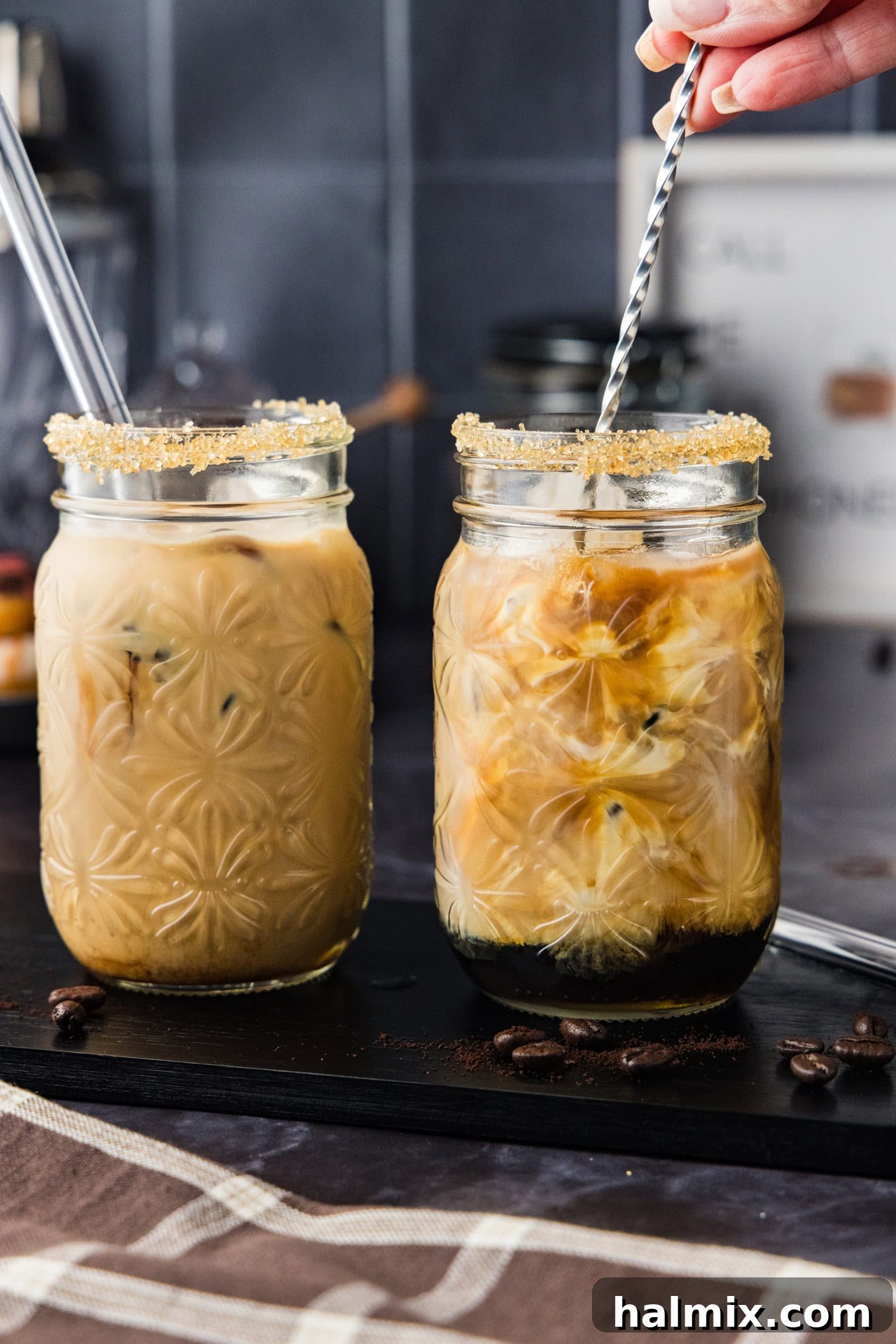 Hand using a cocktail stirrer to mix iced espresso cocktail together in a glass