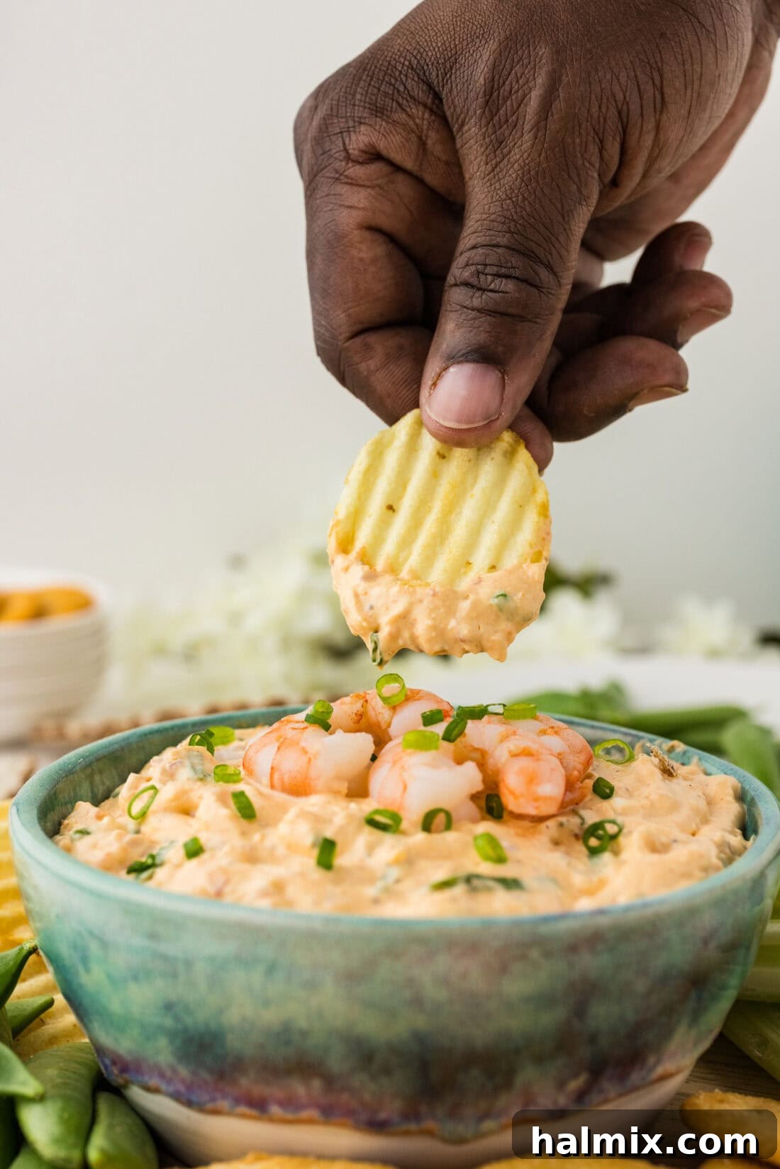 Hand holding a chip with a generous scoop of creamy shrimp dip on it.