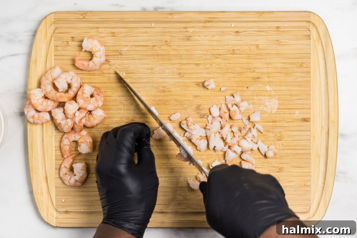 Hands using a knife to chop up shrimp on a cutting board, preparing them for the dip.